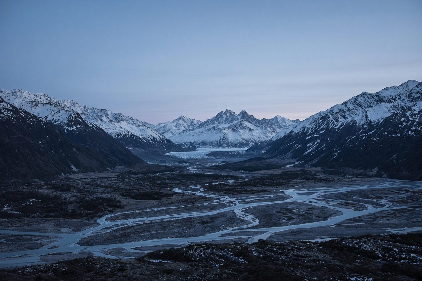 Alaskan glacial valley at blue hour, a braided river under distant snow peaks.
